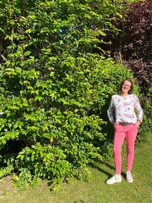 Andrea Heumann steht vor einer grünen Hecke