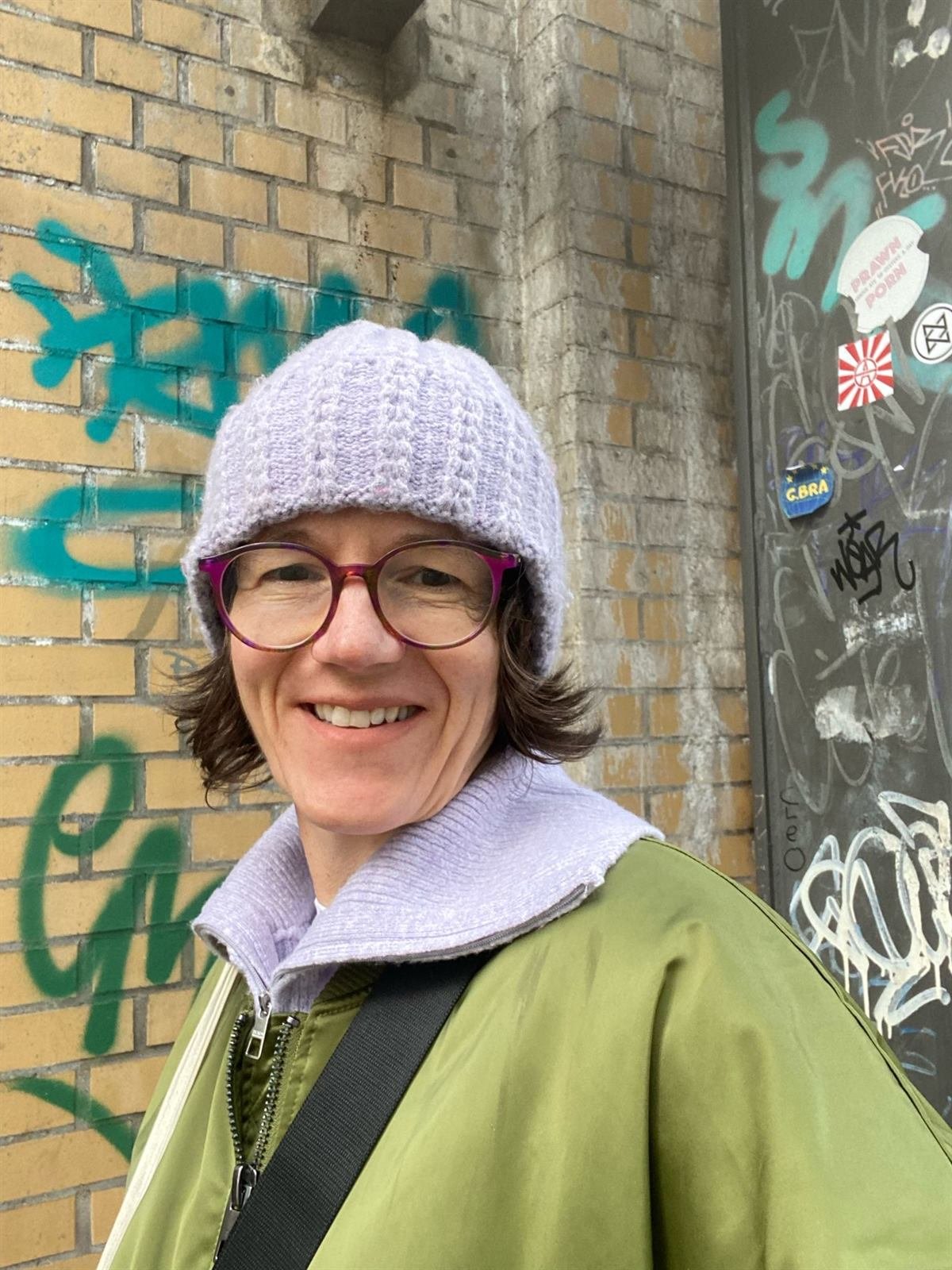 Porträt von Andrea Heumann mit Brille und Mütze, herzlich lächelnd