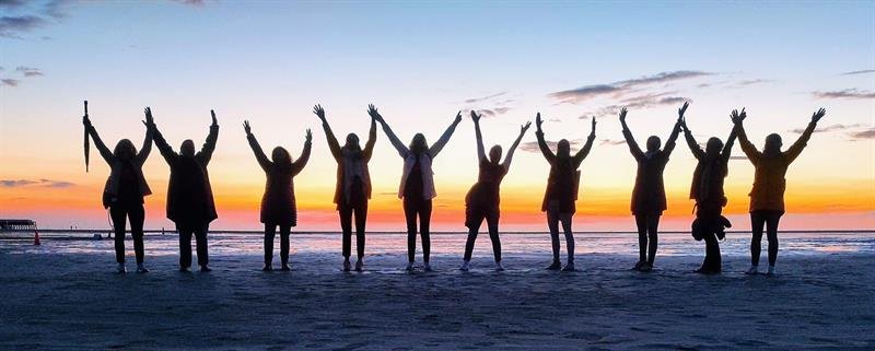 Silhouetten einer Gruppe mit erhobenen Armen im Sonnenuntergang am Strand