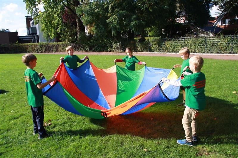 Kinder spielen mit einem bunten Schwungtuch auf einer Wiese